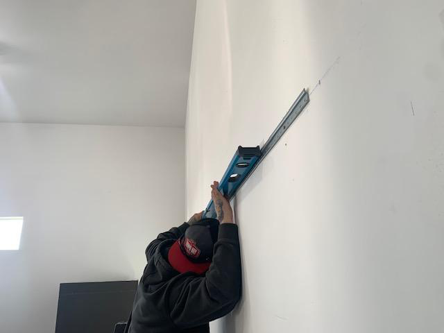 Person drilling rail into wall with level